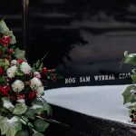 Snow-covered tombstone with red roses and white flowers, symbolizing winter's serene beauty in a cemetery.